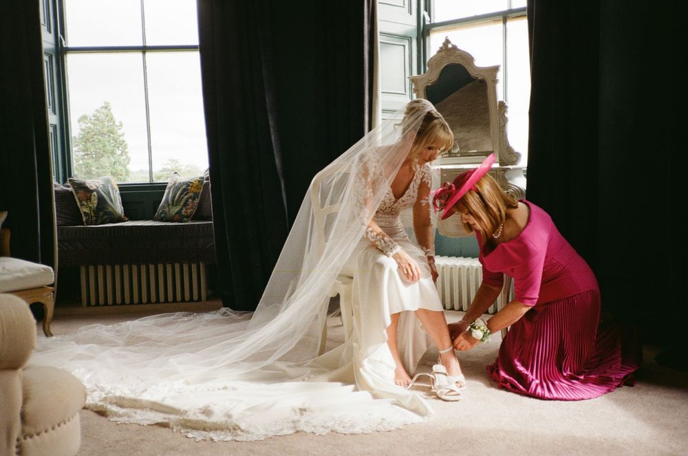 A wedding dress with flowing veil creates an ethereal silhouette against sunlit windows in an elegant indoor setting.