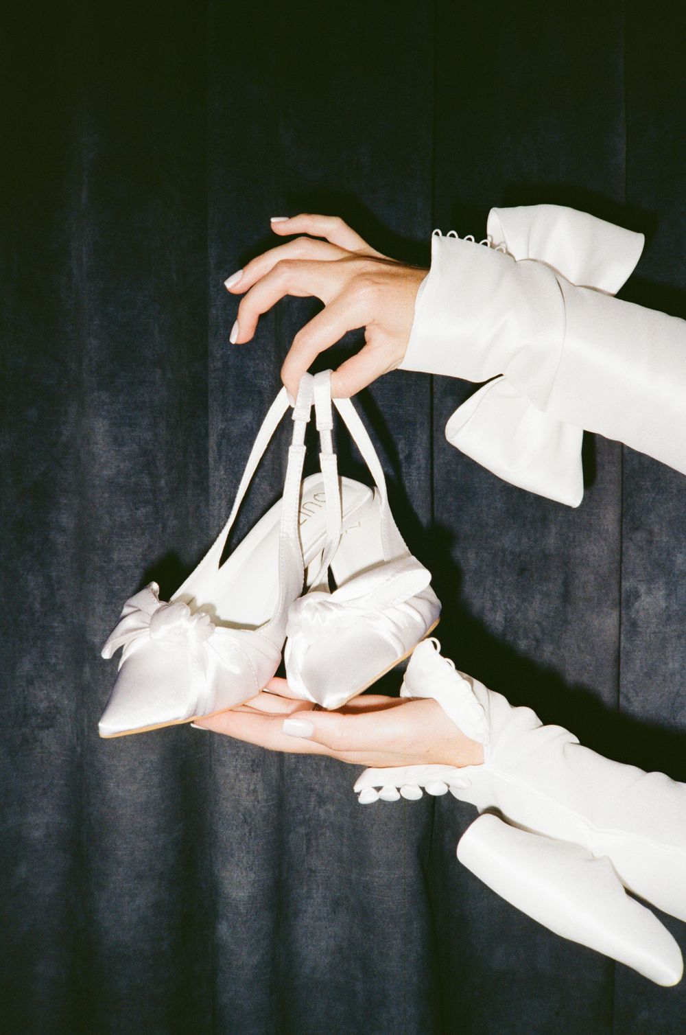 A sequence of hands holding and manipulating white high heeled shoes against a dark background.