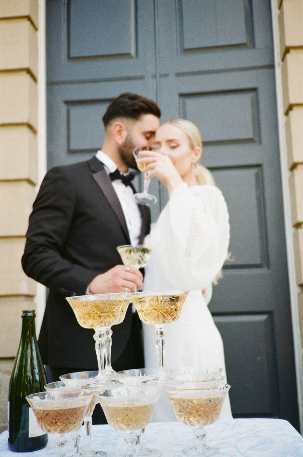 Champagne glasses arranged in a tower formation at an elegant wedding reception with guests in formal attire.