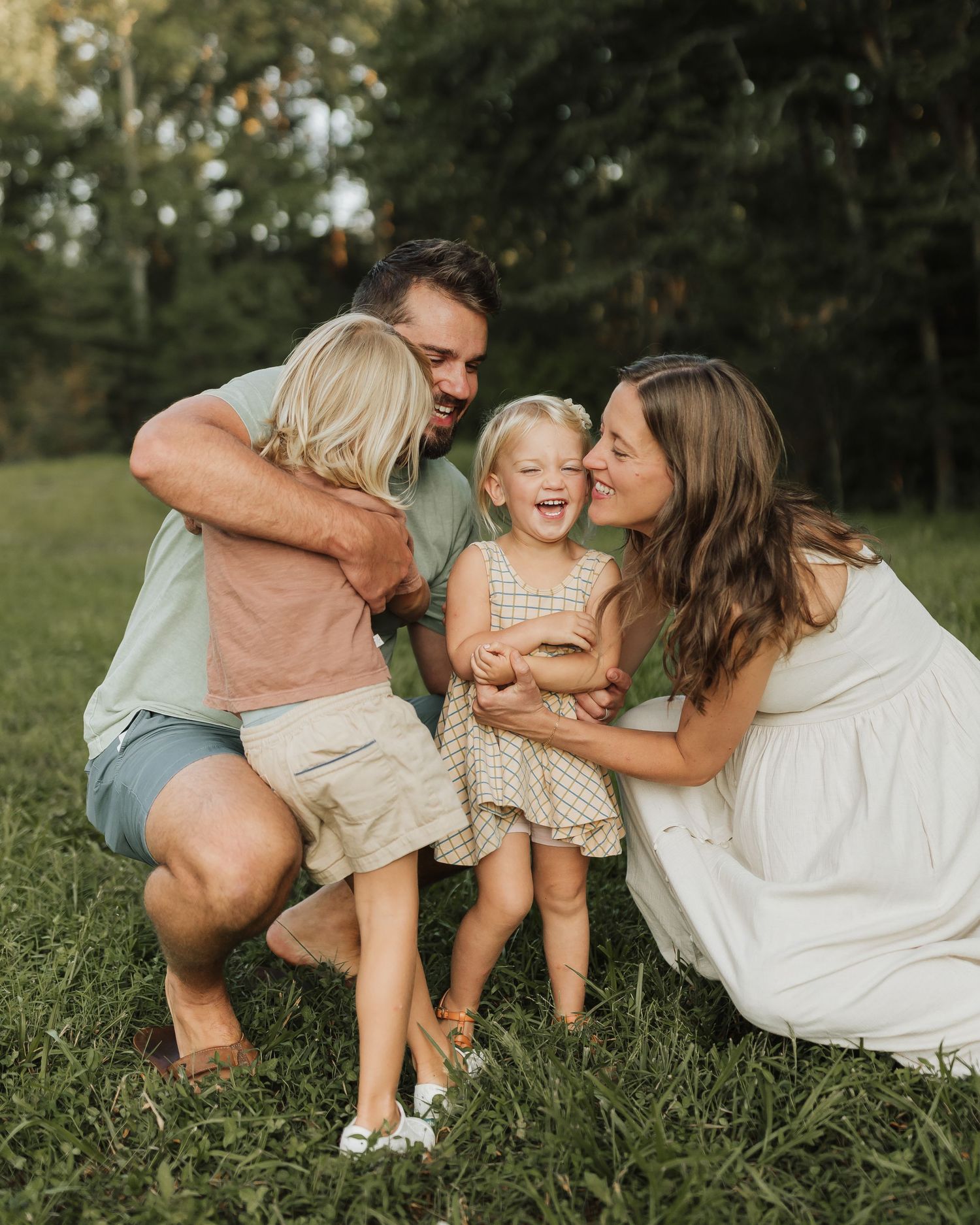 A loving family shares joyful moments together while sitting on green grass in a sunlit outdoor setting.