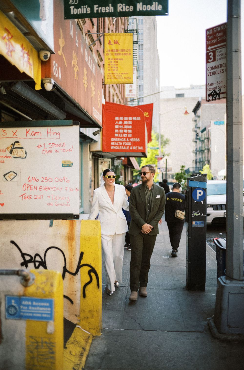 Two people walk past Asian restaurants and street art in an urban neighborhood.