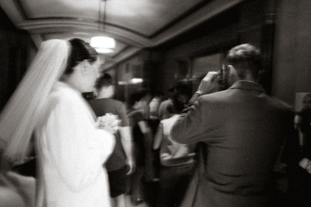A blurred black and white photo of a wedding celebration with a photographer capturing the moment.