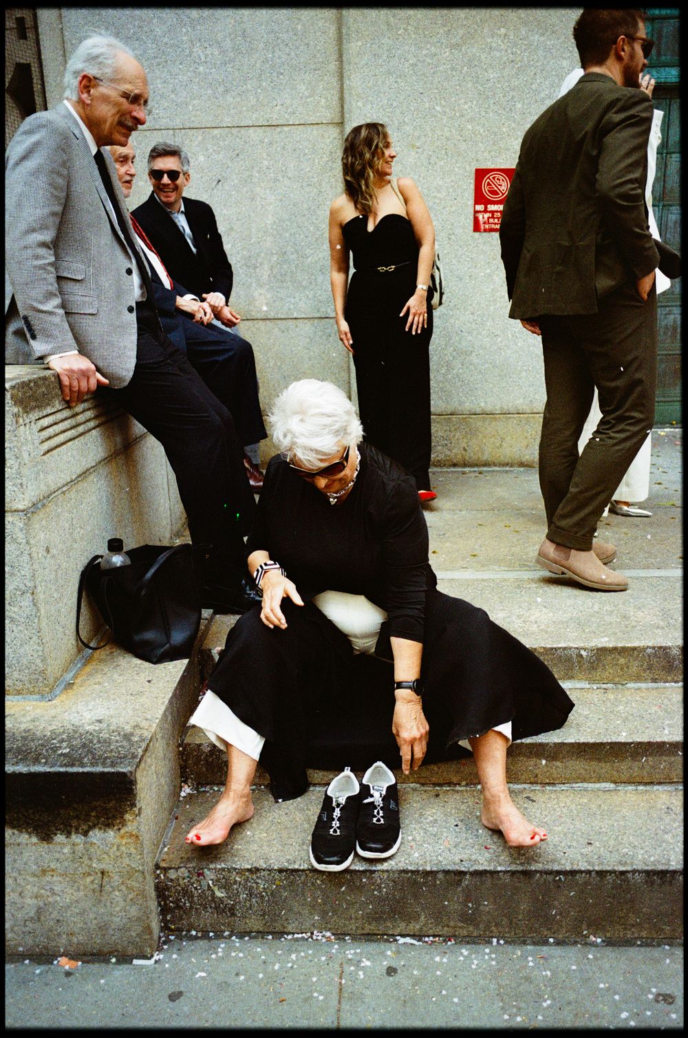 Urban street scene with people sitting on concrete steps in casual attire.