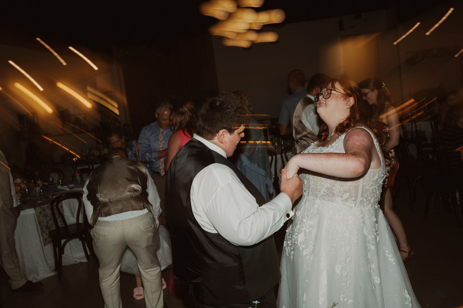 Party goers dance and celebrate with raised hands inside a dimly lit brick-walled venue.