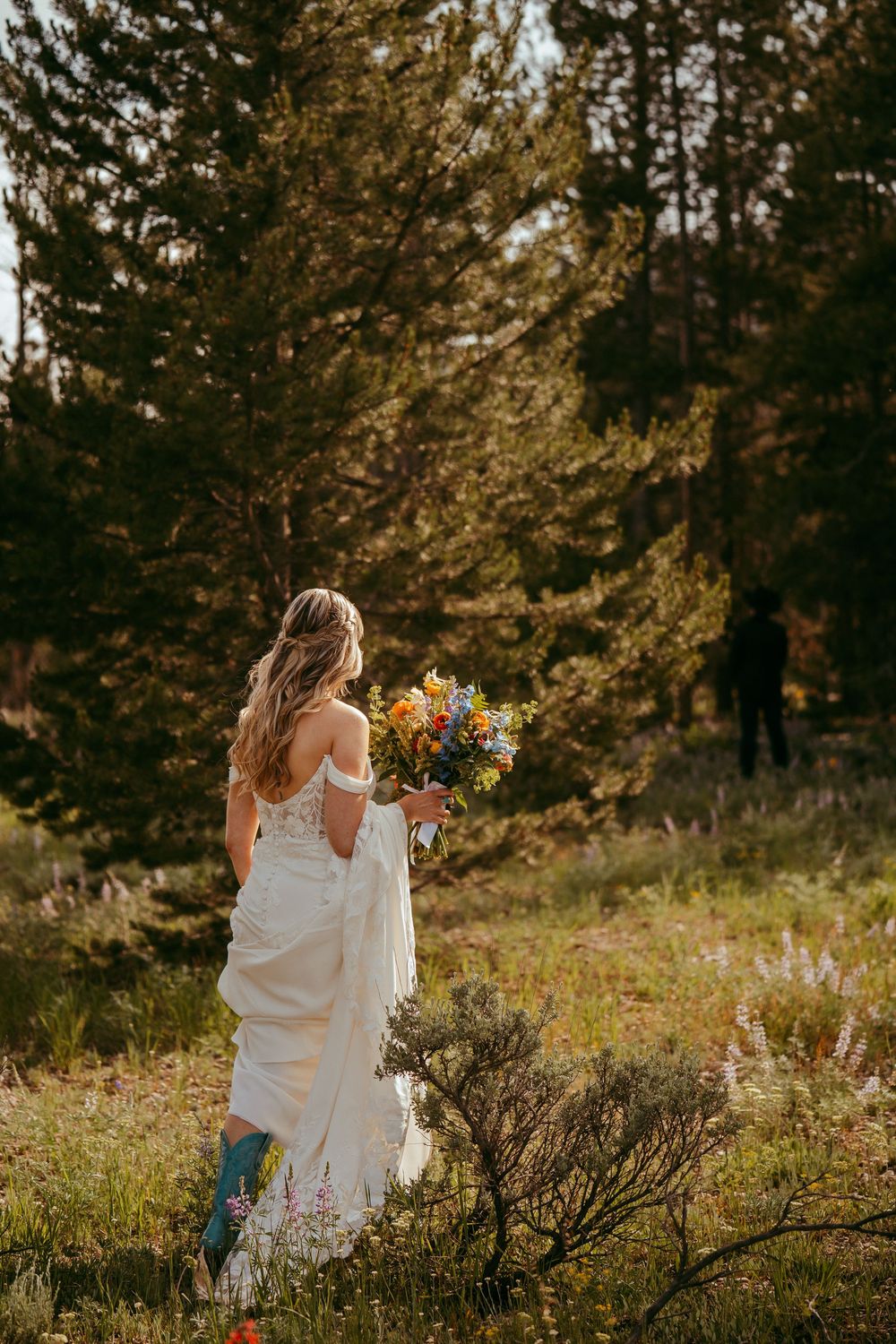 Rustic mountain wedding ceremony with a bride and groom exchanging vows in a wildflower meadow, surrounded by pine trees and mountains