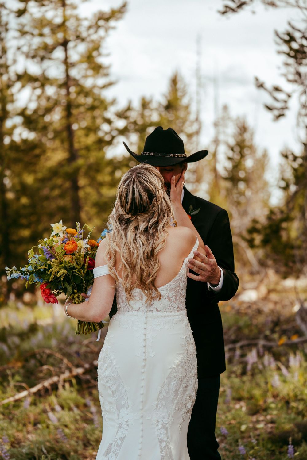 Rustic mountain wedding ceremony with a bride and groom exchanging vows in a wildflower meadow, surrounded by pine trees and mountains