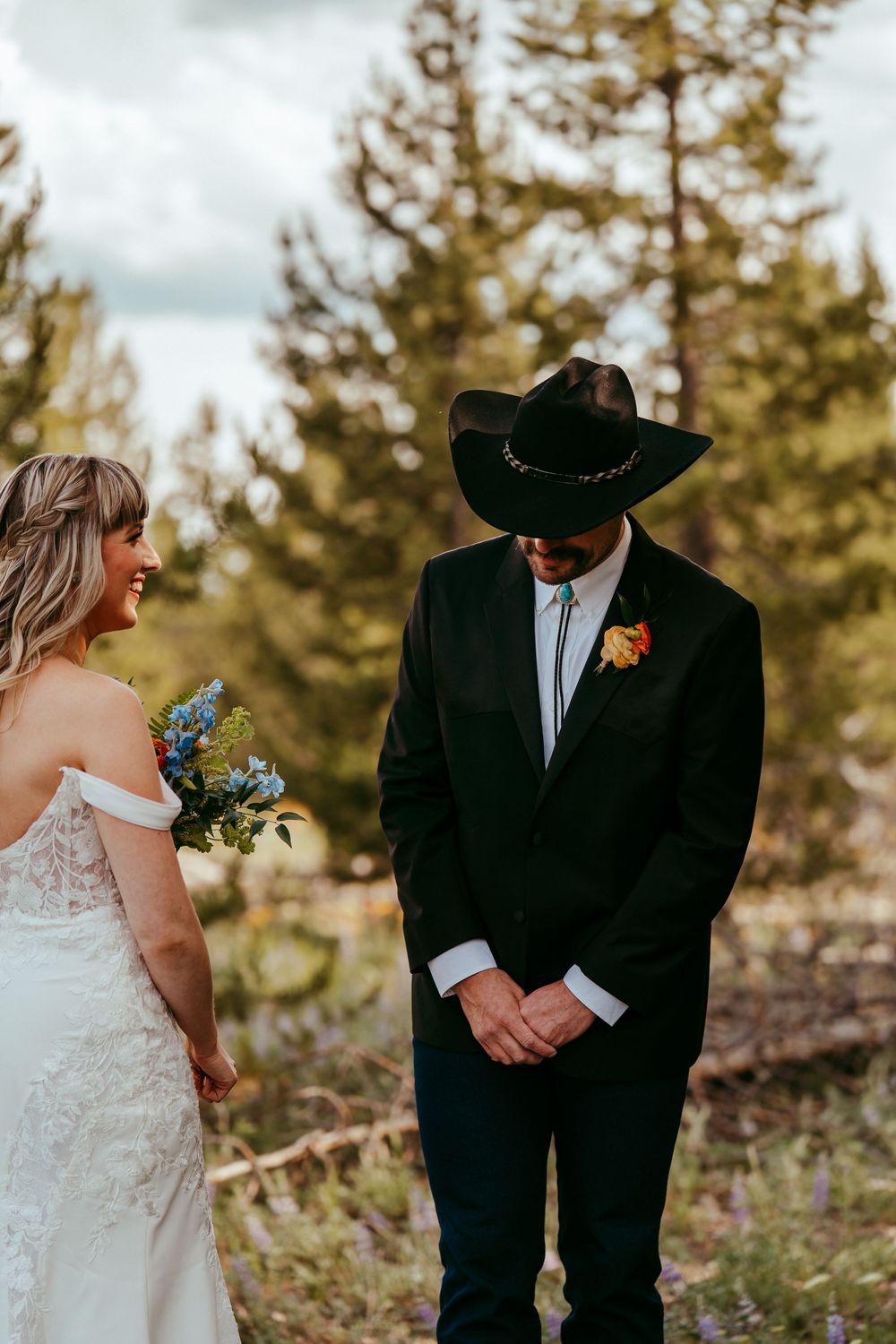 Rustic mountain wedding ceremony with a bride and groom exchanging vows in a wildflower meadow, surrounded by pine trees and mountains