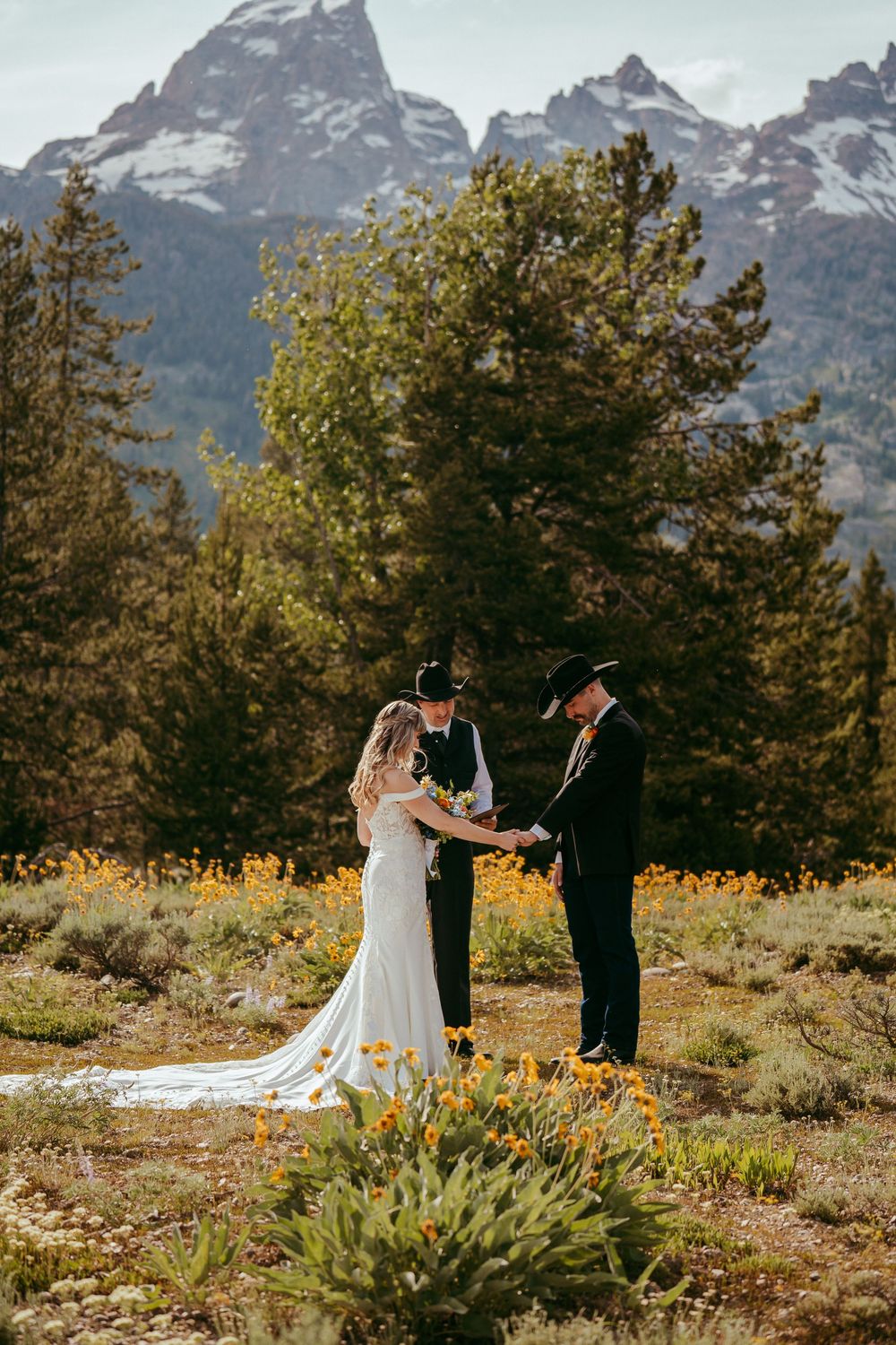 Rustic mountain wedding ceremony with a bride and groom exchanging vows in a wildflower meadow, surrounded by pine trees and mountains