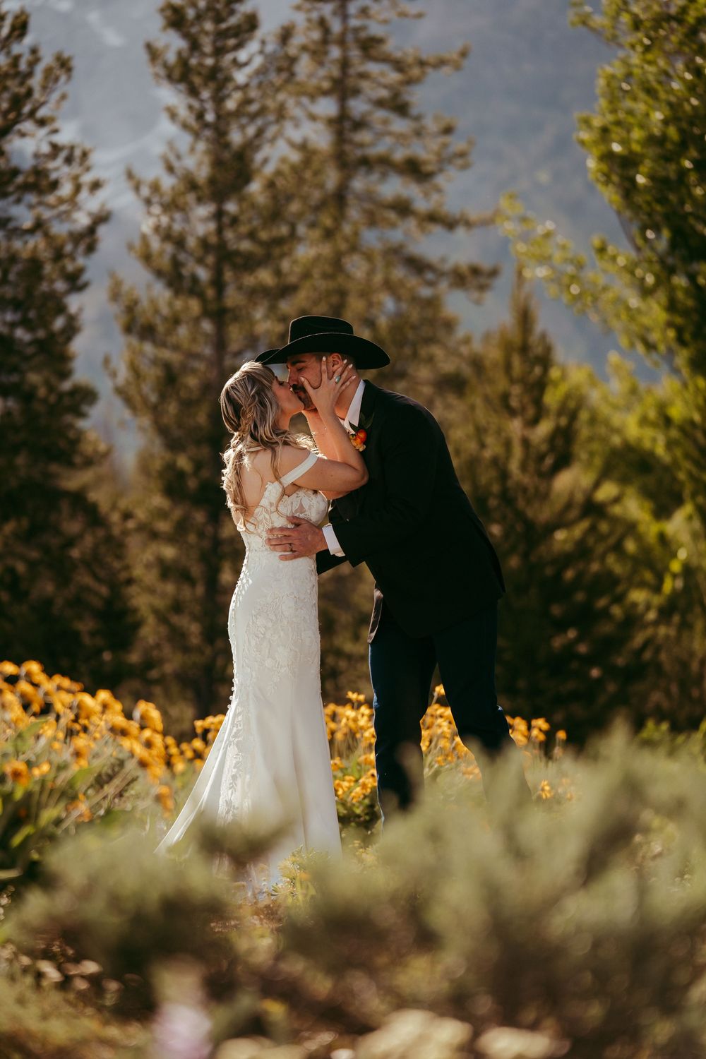 Rustic mountain wedding ceremony with a bride and groom exchanging vows in a wildflower meadow, surrounded by pine trees and mountains
