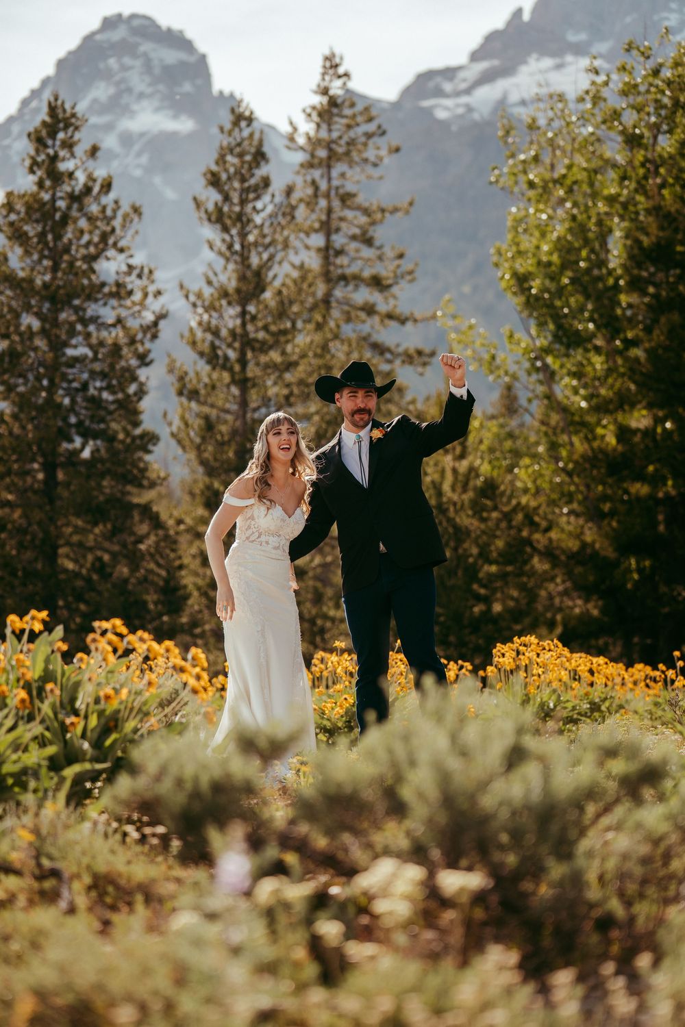 Rustic mountain wedding ceremony with a bride and groom exchanging vows in a wildflower meadow, surrounded by pine trees and mountains