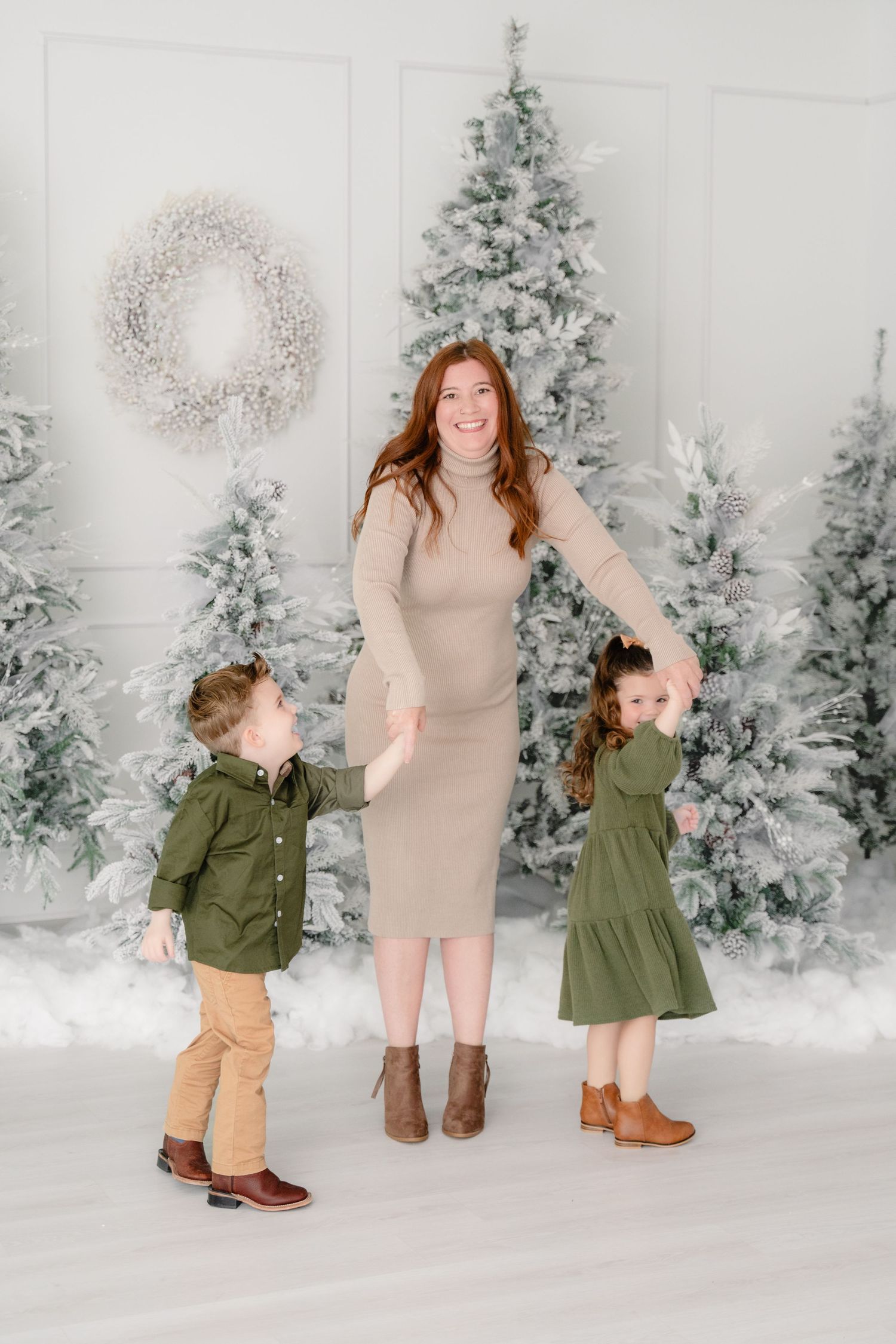 Three joyful figures dance together in matching winter outfits against a snowy backdrop with frosted Christmas trees.