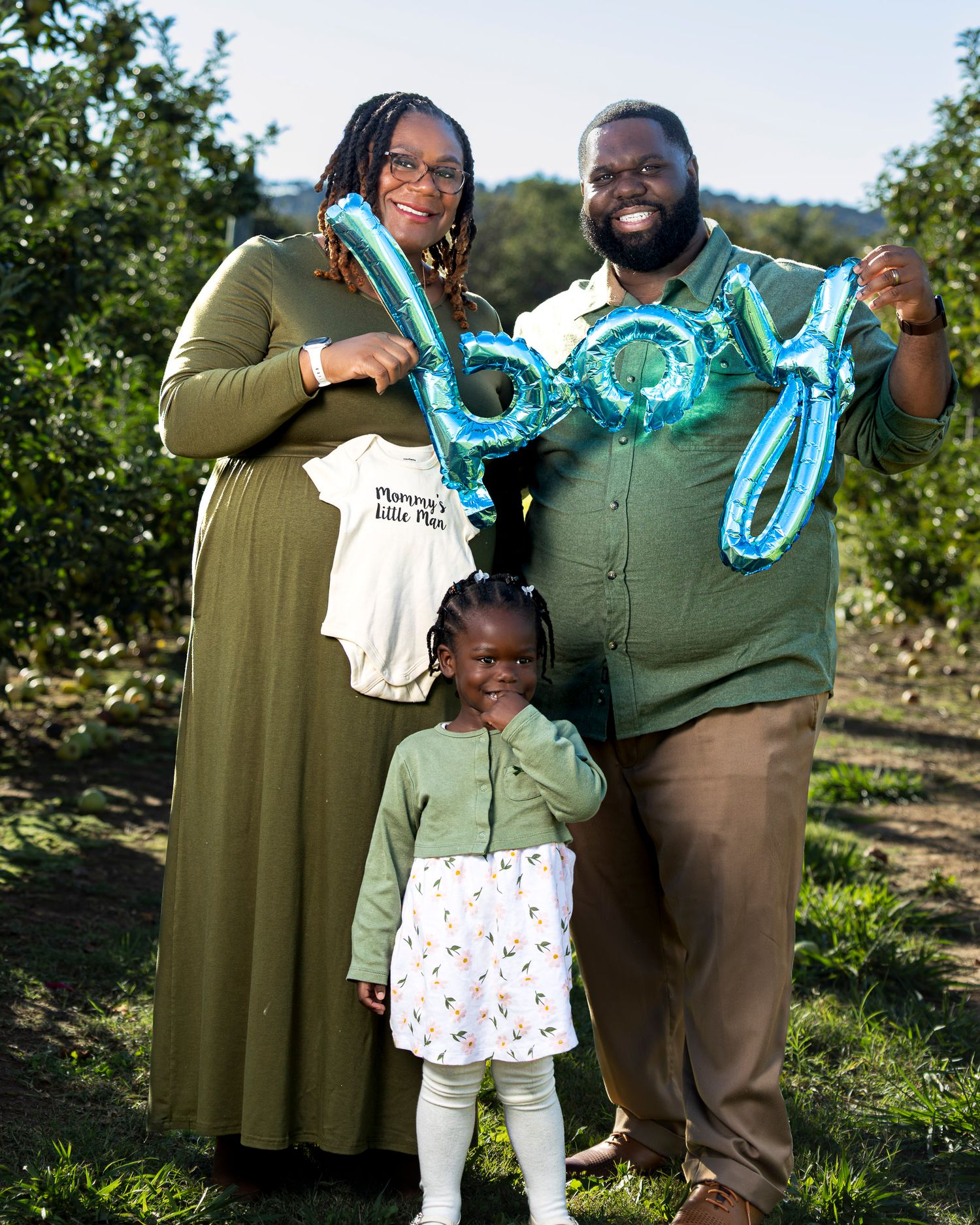 A parent and child celebrate a birth announcement outdoors with blue balloon decorations on a sunny day in Fayetteville AR