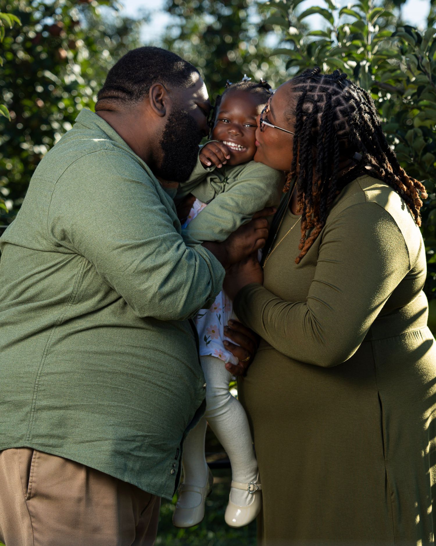 A family in matching olive green outfits share a warm moment outdoors at Rivercrest Orchard in Fayetteville AR