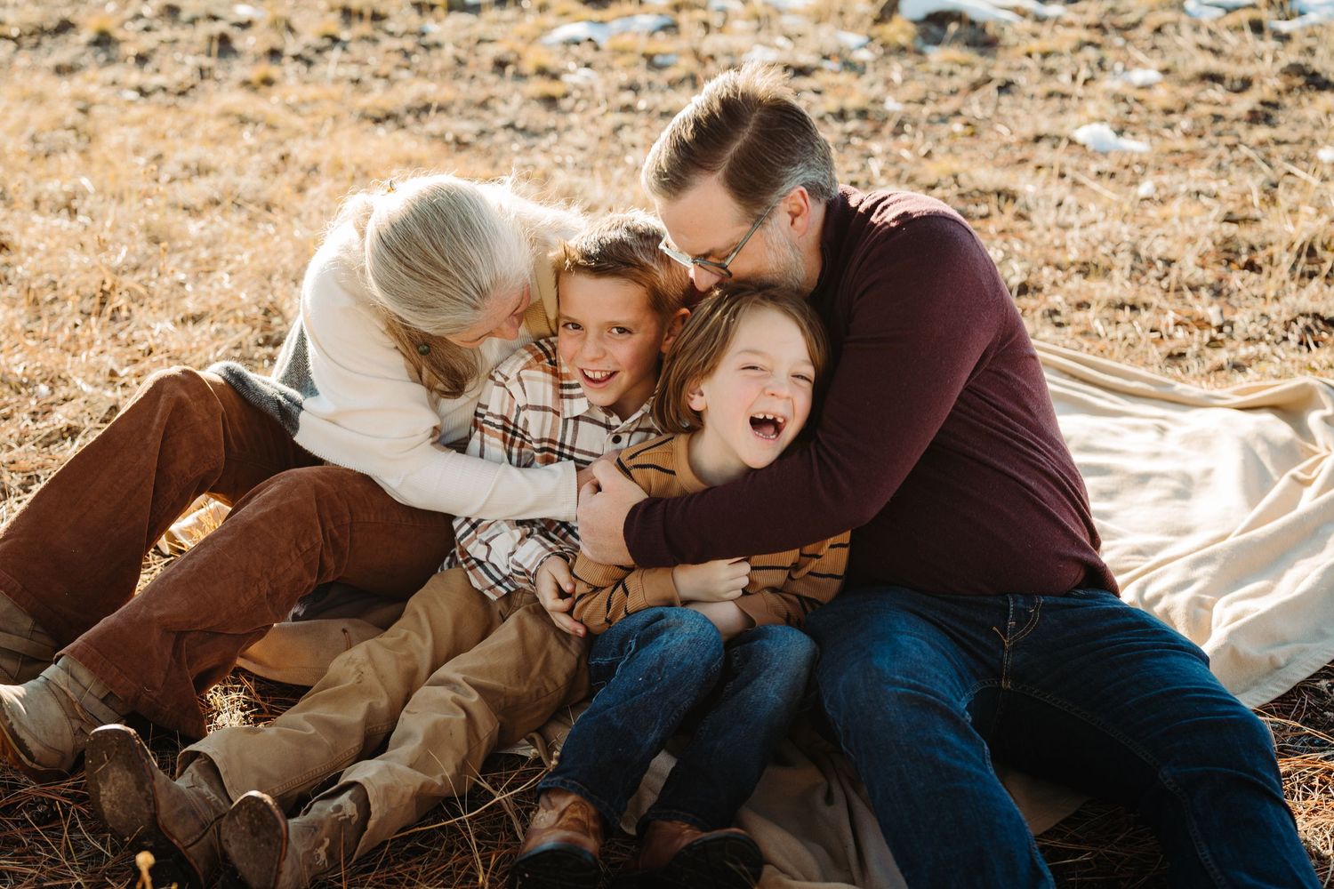 A family shares a joyful moment together while sitting on a blanket outdoors on rocky ground in warm sunlight.