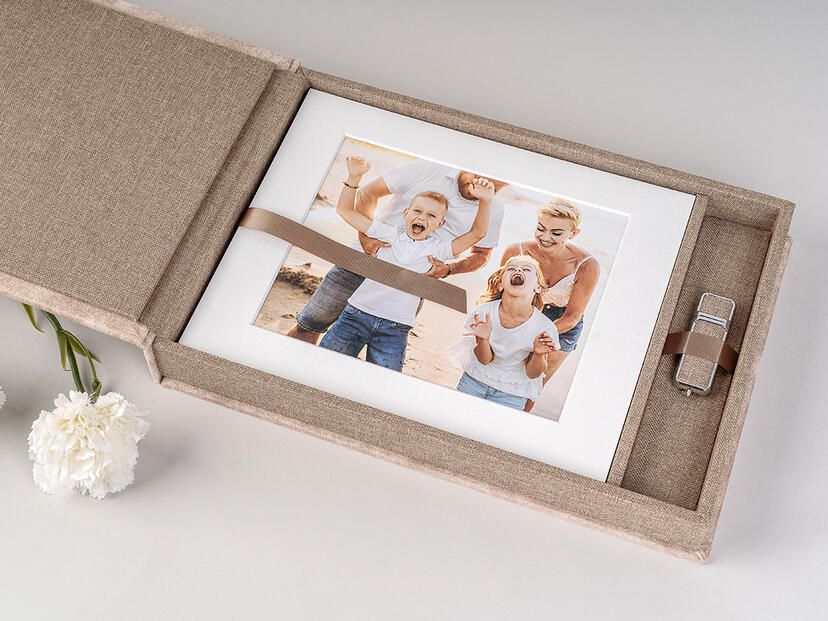 Modern wooden frames with wedding photos arranged horizontally on a neutral grey wall with white flowers as decor.