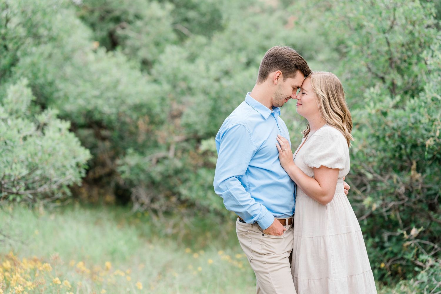 Two people embracing in a romantic pose against a lush green garden background in natural light.