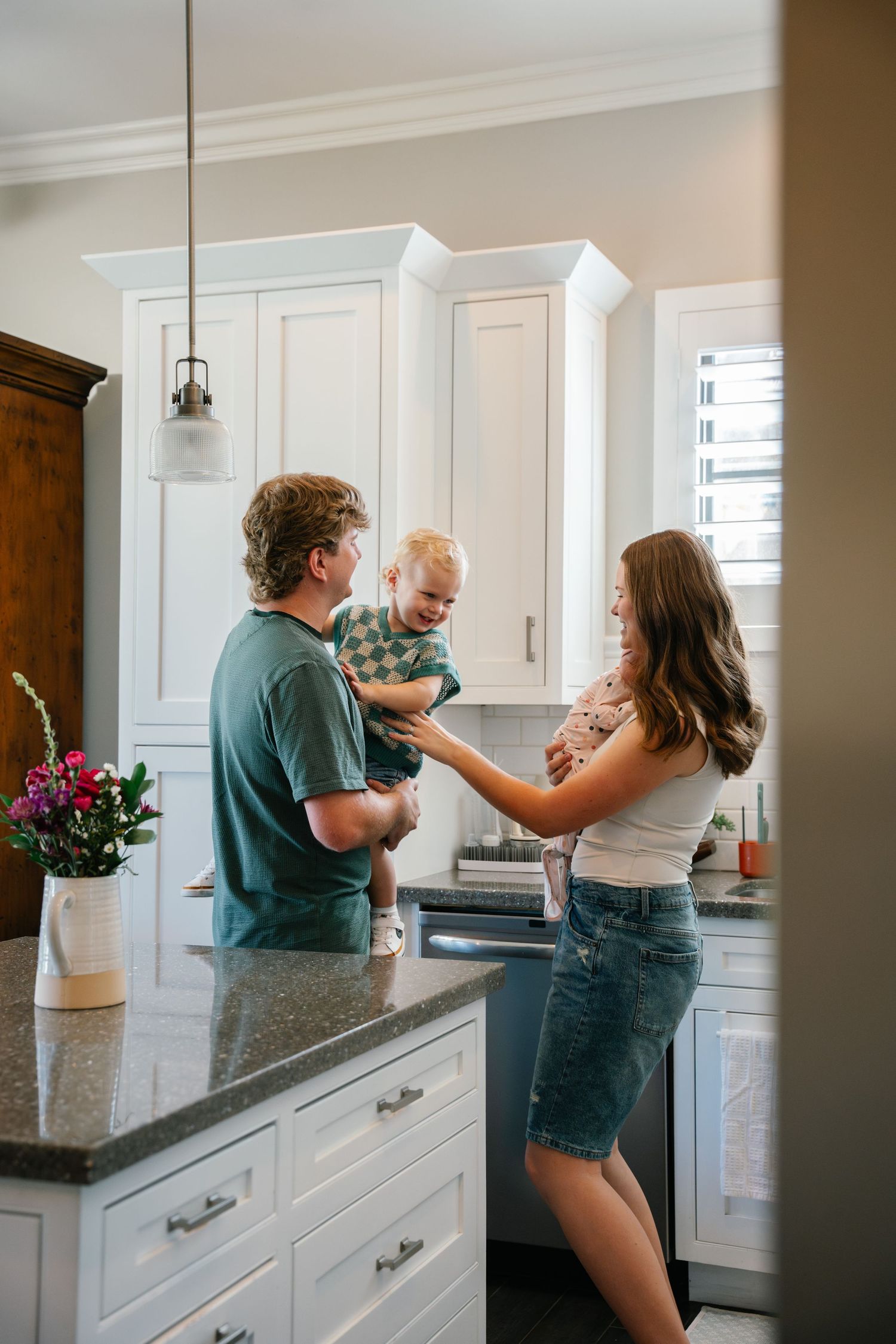 Heartfelt Des Moines family session: parents and toddler sharing joyful moment in home kitchen