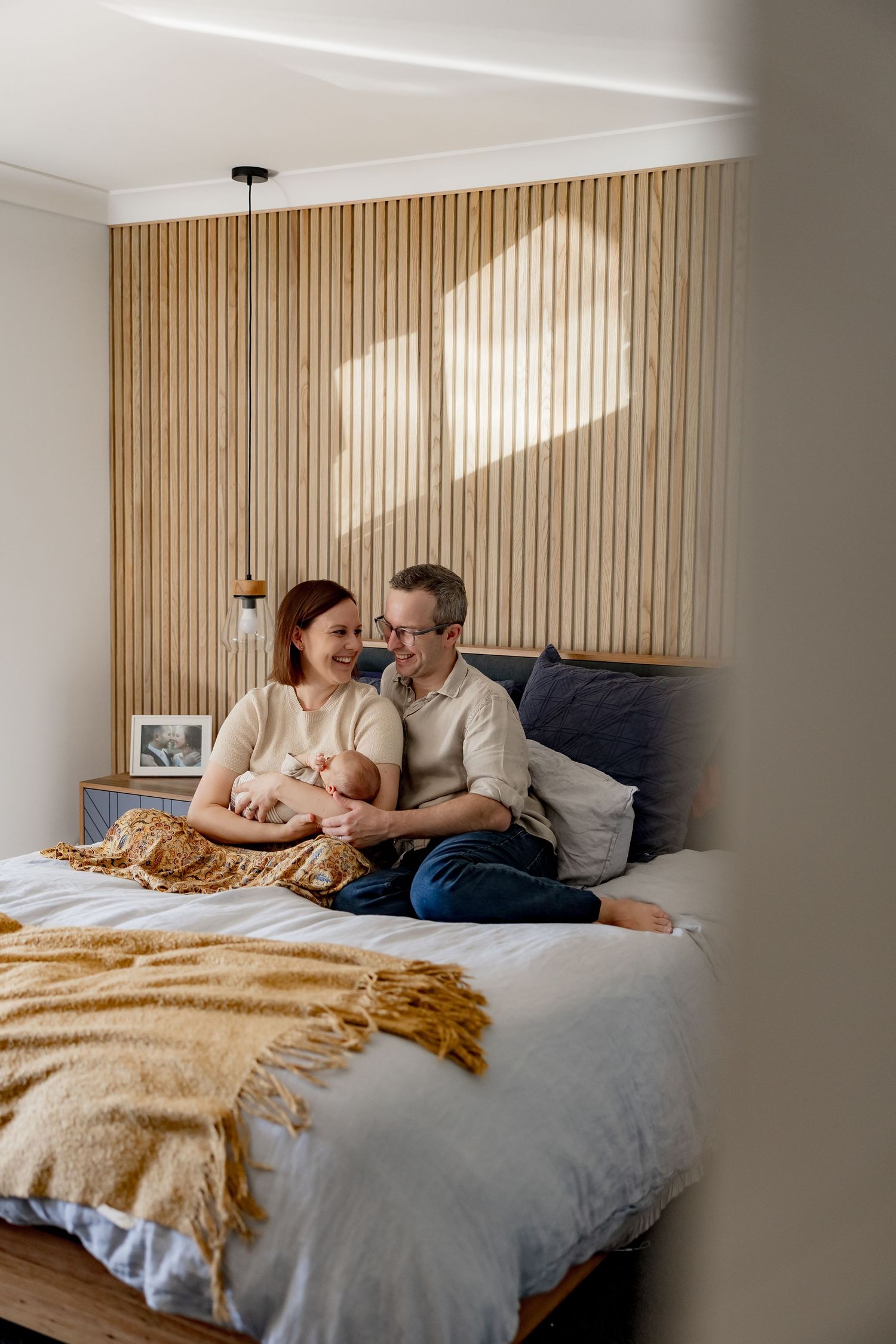 A cozy bedroom scene with a modern wood slat wall and warm mustard throw blanket on a gray bed.