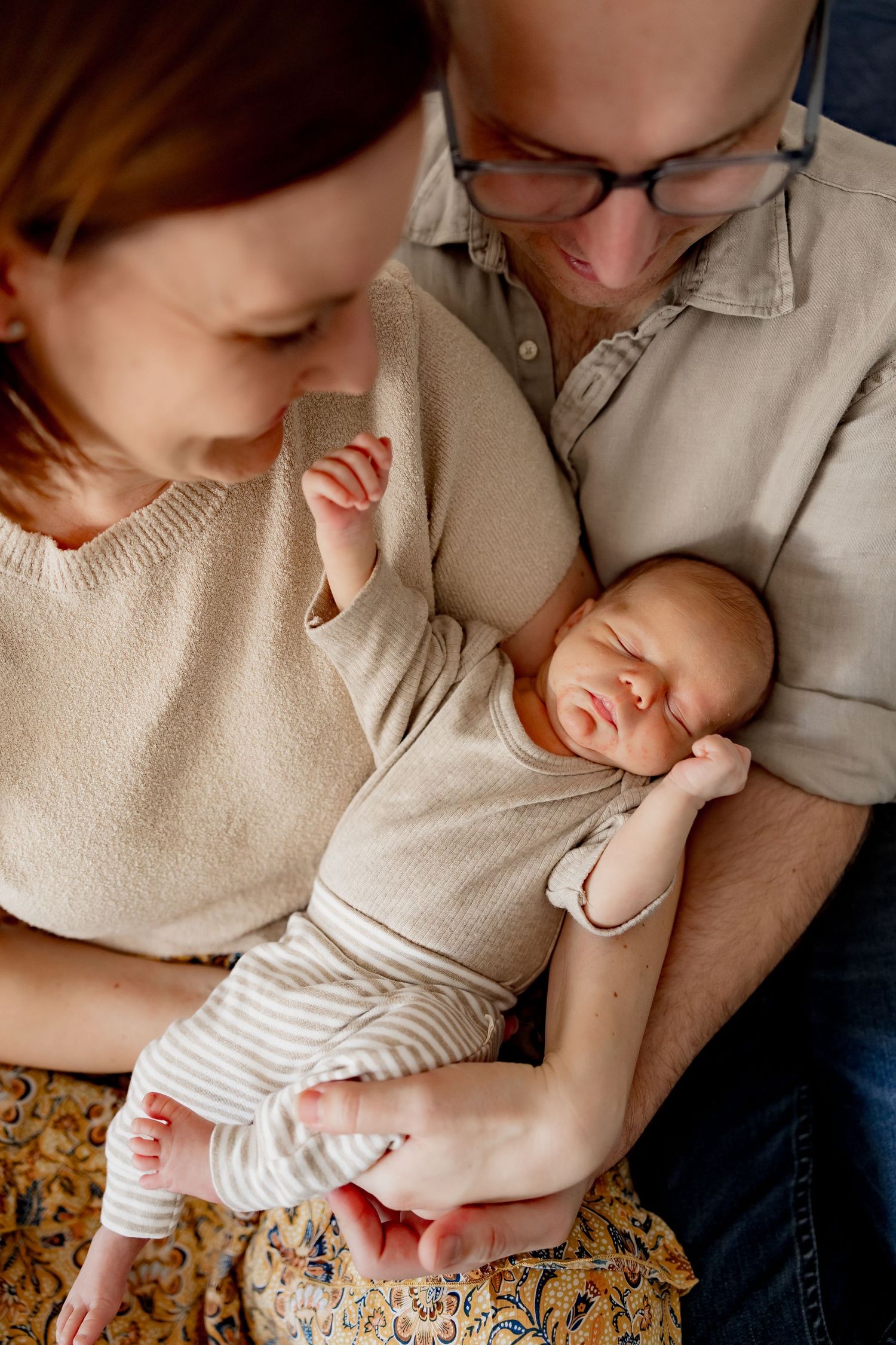 A newborn baby in a white striped onesie being cradled gently in their parents' arms.