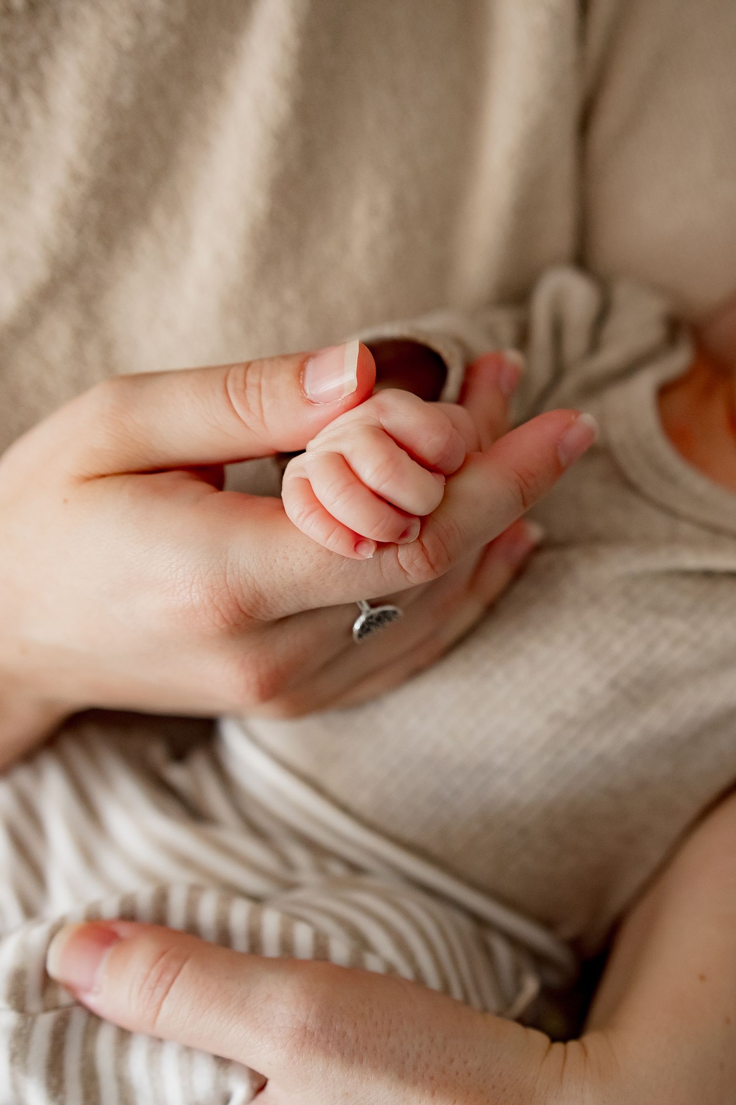 Close-up view of tiny baby fingers gently reaching against a soft beige blanket in natural light.