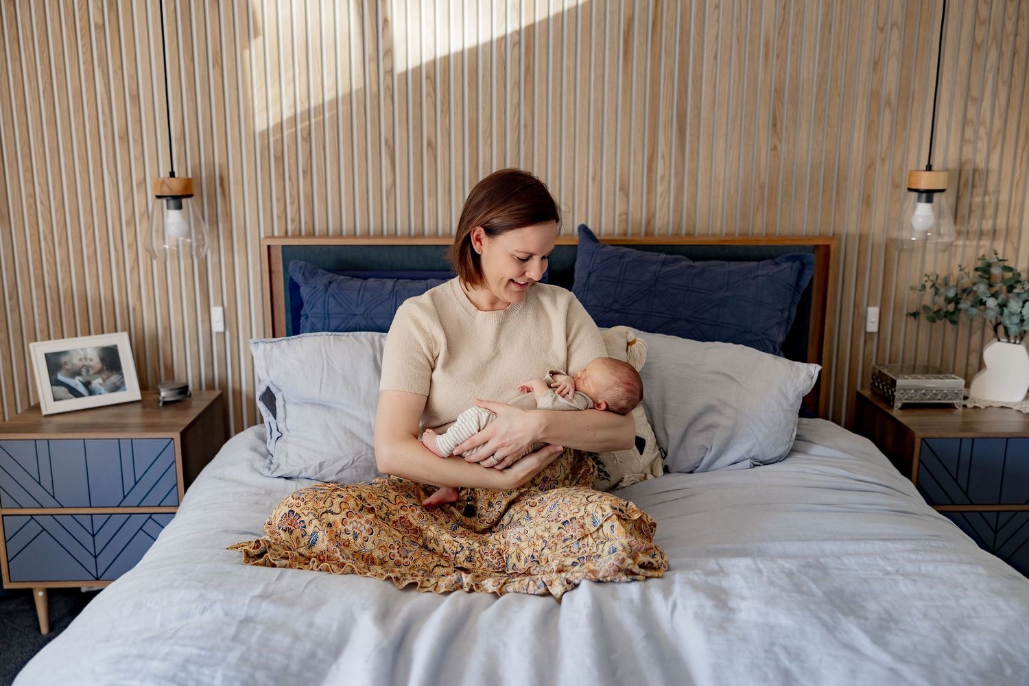 An infant resting peacefully on a bed with parents nearby in a sunlit room.