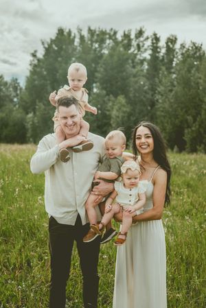 A group in light-colored clothing stands together in a tall grass field on a summer day. St Albert Family Photographer