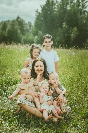 A family sits together in a sunny meadow surrounded by tall grass and wildflowers on a summer day. St Albert Family Photographer
