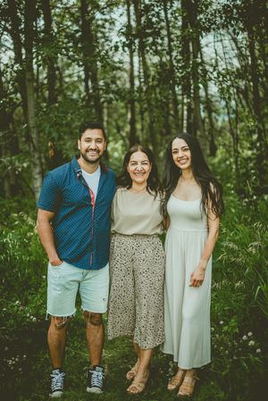 Three people standing and smiling in a lush forest setting during summer, wearing casual outdoor attire. St Albert Family Photographer