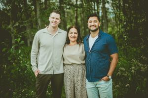Three people pose together for a casual outdoor portrait in front of a wooded backdrop. St Albert Family Photographer