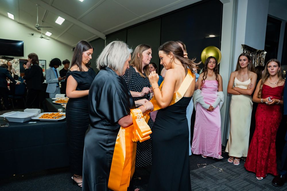 A group of people in formal attire gather at an evening event with a buffet table and dark background.
