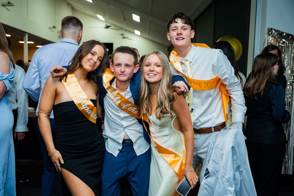 A group of students celebrating at a school dance wearing formal attire and decorative sashes.