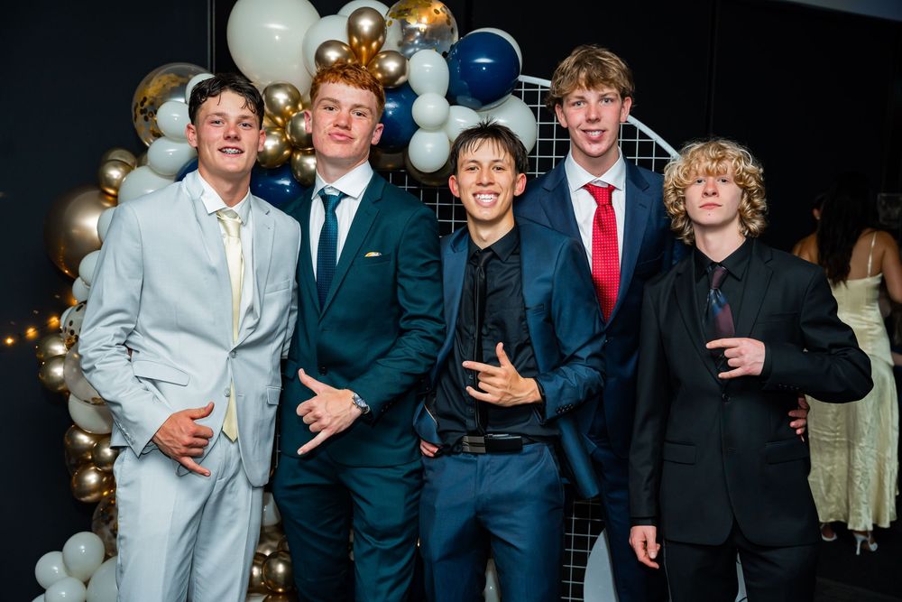 A group of groomsmen posing together at a wedding reception wearing navy suits and red ties.
