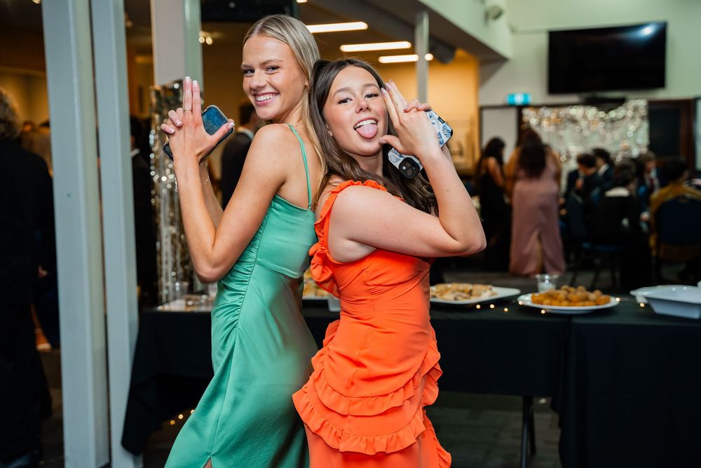 Two guests in bright turquoise and orange dresses strike playful poses at a party event.