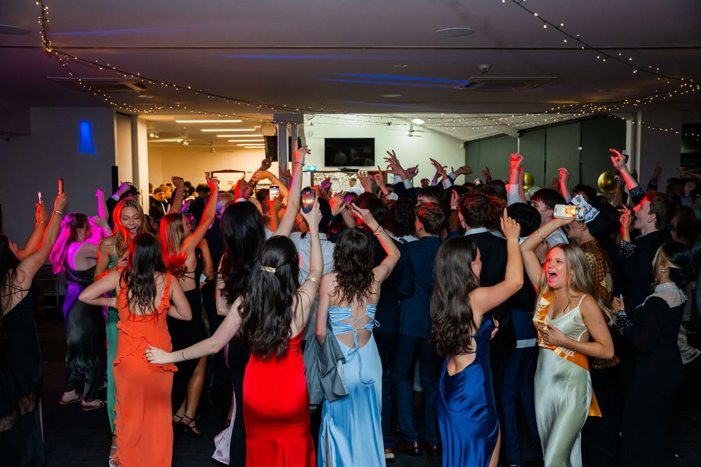Wedding reception guests dancing and celebrating on a lively dance floor under dim lights at a nightclub or venue.