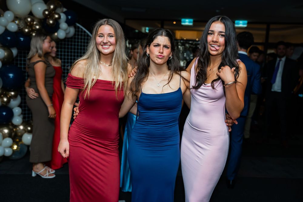 Three friends pose together at a formal event wearing elegant fitted dresses in red, blue and lavender colors.