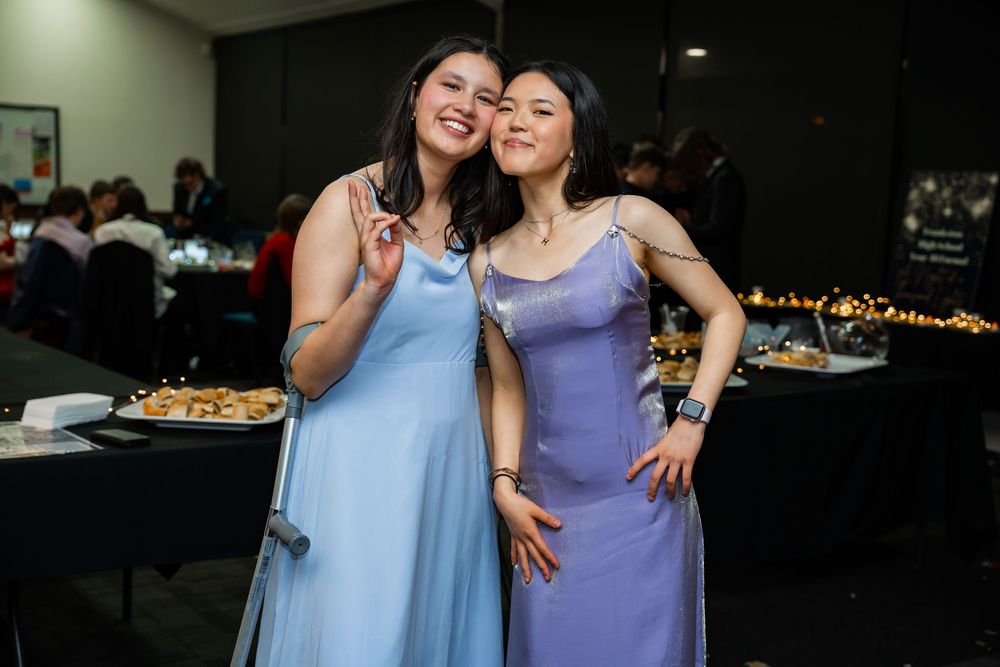 Friends in blue and purple dresses share laughs and smiles at what appears to be a festive evening event.