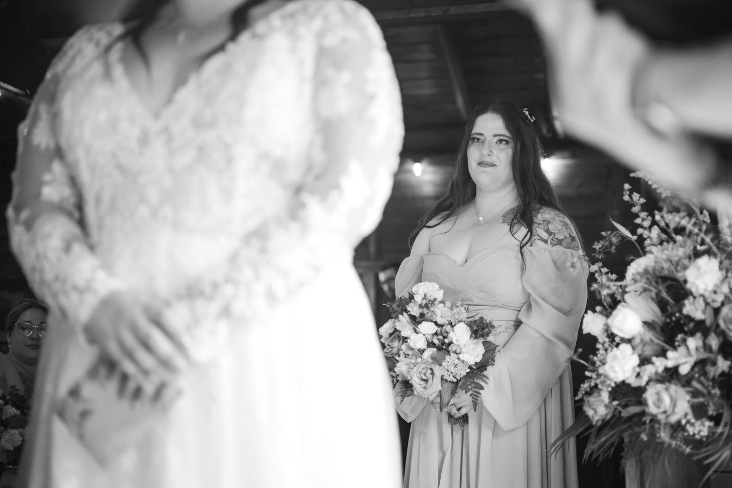 A black and white wedding photo showing people in formal wear holding floral bouquets during a ceremony.
