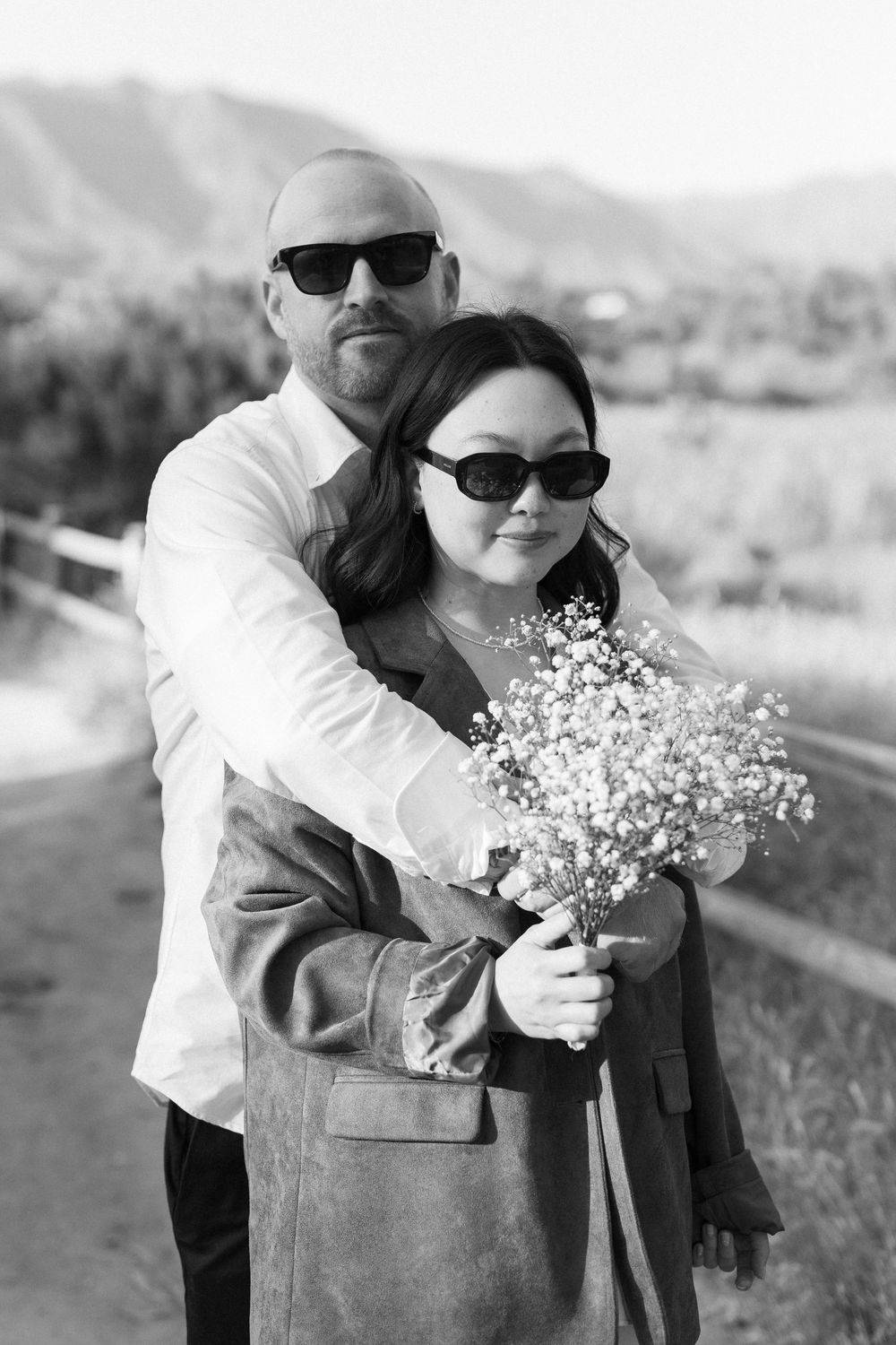 Editorial-style black and white film image of couple wearing sunglasses in a sunlit Ojai field.
