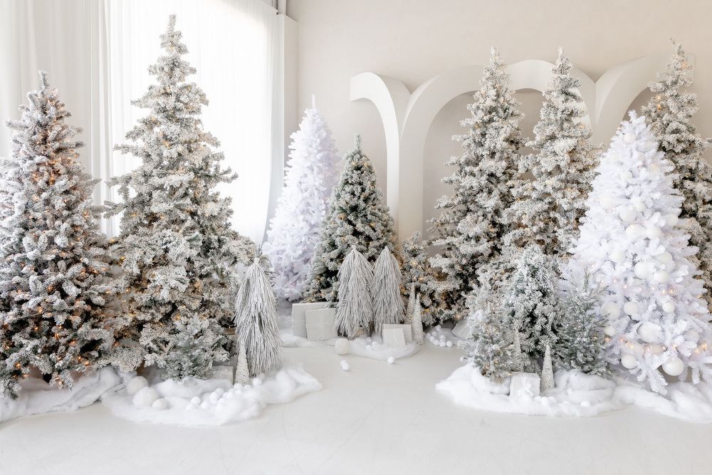 Multiple flocked Christmas trees arranged in an elegant white room with arched doorways.