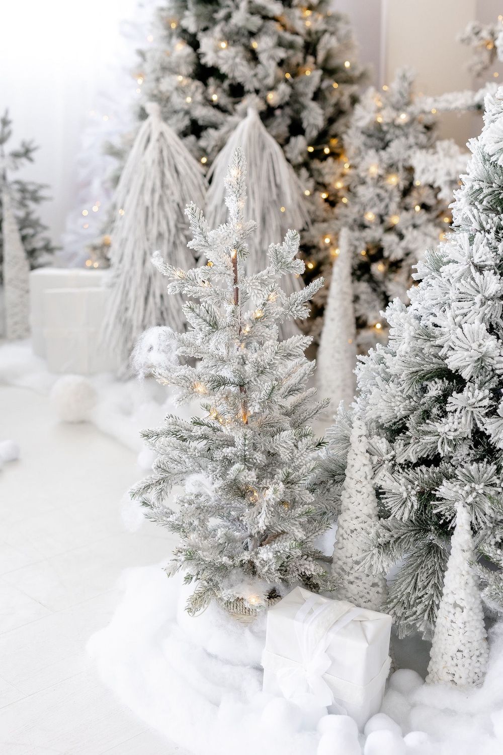 Close-up of flocked white Christmas trees with sparkling lights and festive decorations in winter display setting.