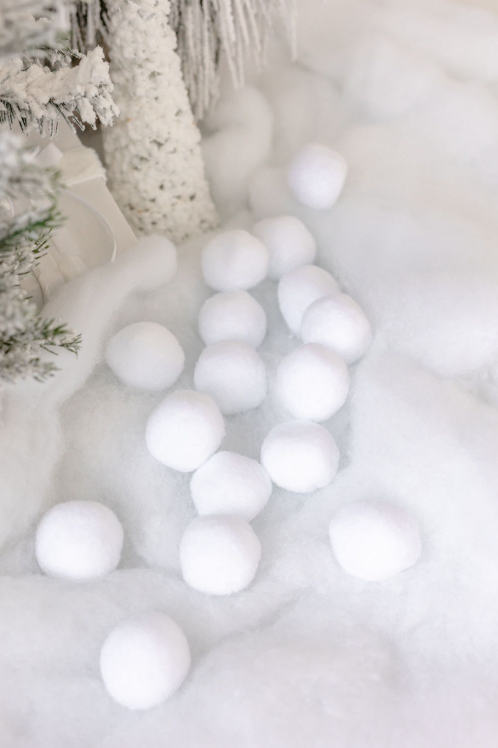 White decorative snowballs scattered on fluffy white fabric near frosted pine branches.