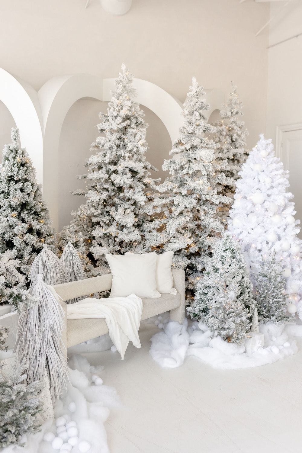 Dreamy white Christmas scene with frosted trees, plush seating, and architectural arches.