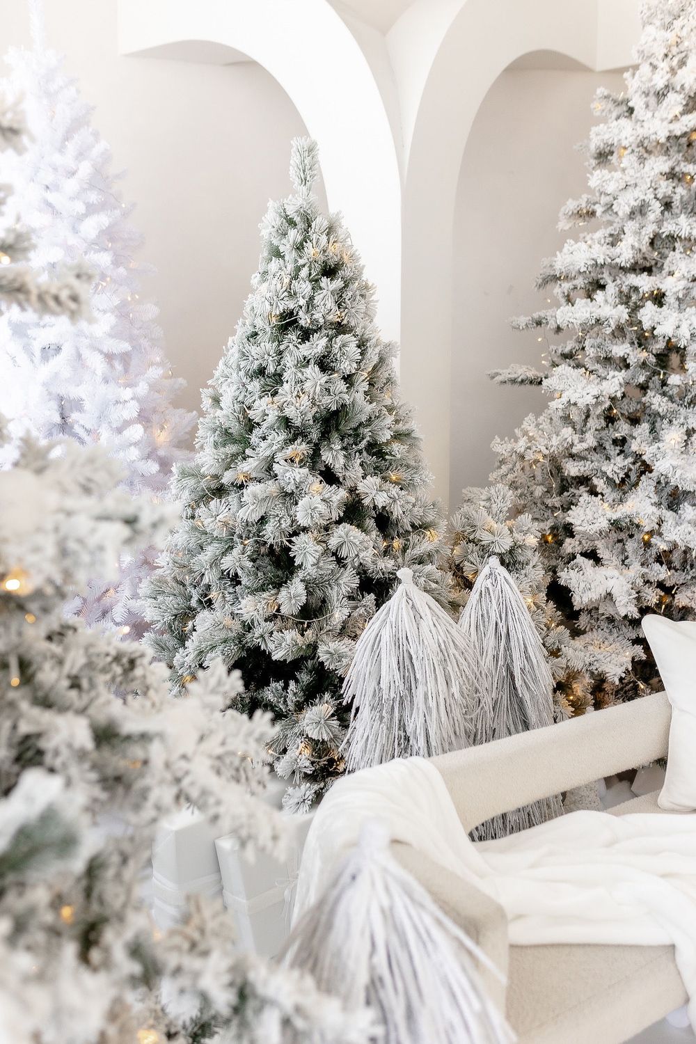 White flocked Christmas trees with tassel decorations in an elegant arched room setting.