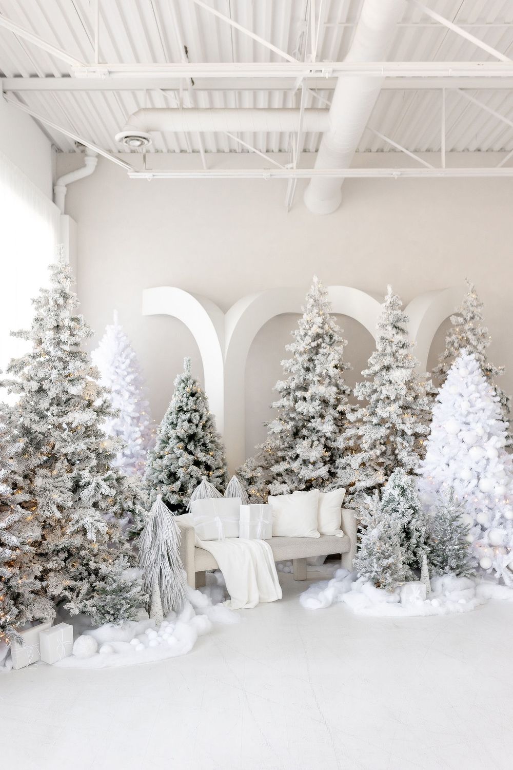 Elegant winter wonderland display with flocked Christmas trees and white seating against arched wall.