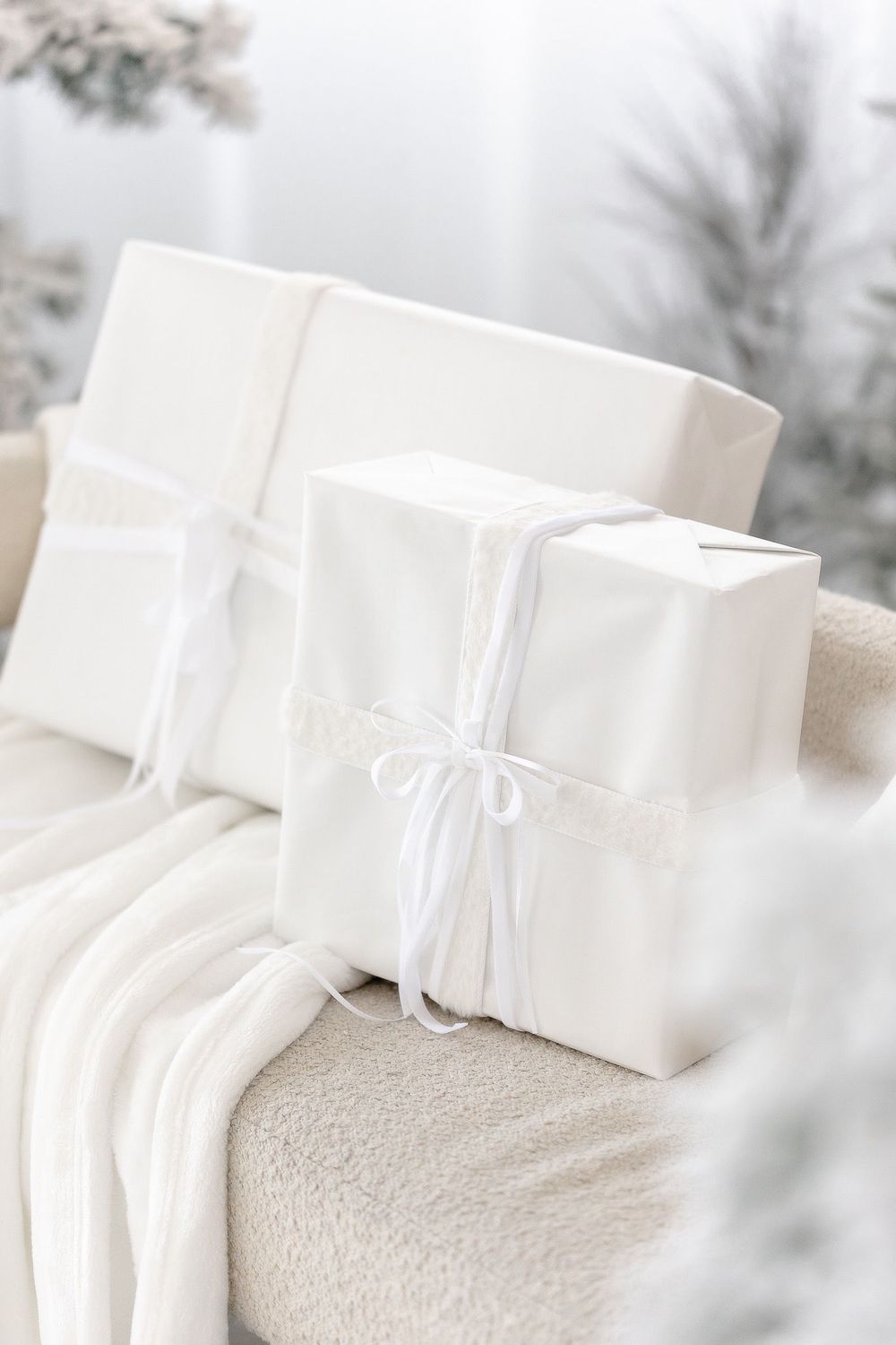 White wrapped presents tied with ribbons on a soft blanket with a dreamy winter background.