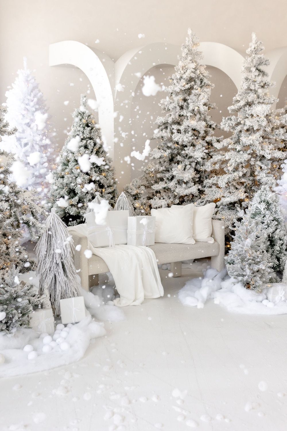 A winter wonderland scene with flocked white Christmas trees and silver decorations in an elegant indoor display setup.