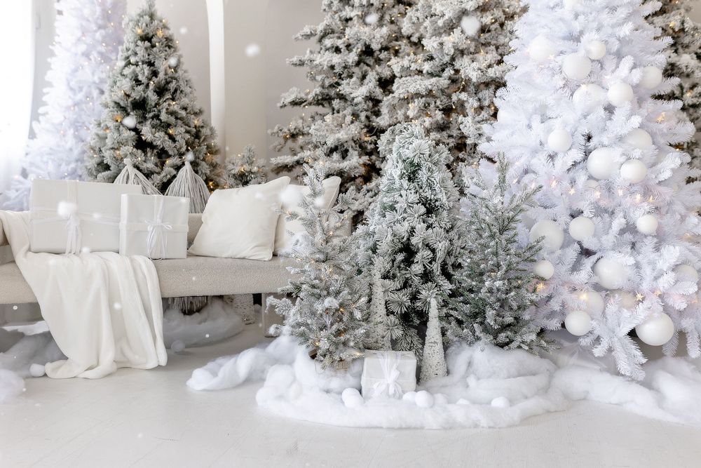 A winter wonderland living room with flocked Christmas trees, white decor, and soft lighting creating a serene holiday scene.