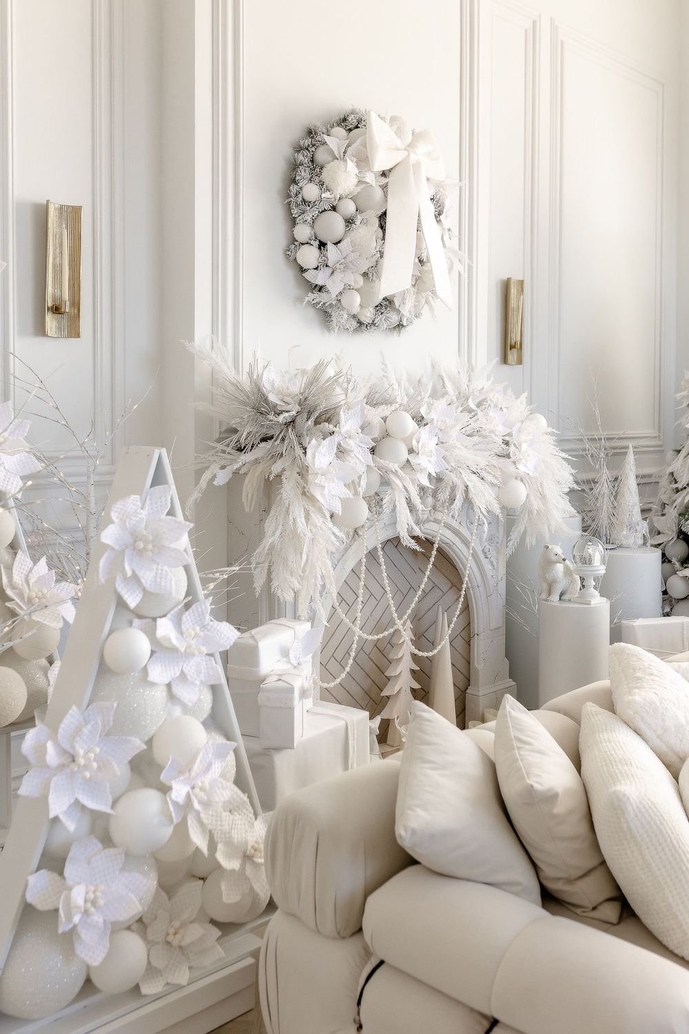 Elegant all-white holiday decor display featuring paper flowers, wreaths, and plush pillows against a light wall.