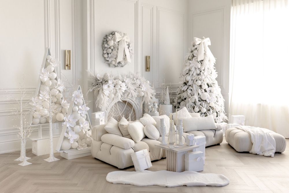 Minimalist white studio set with fabric swatches, presents, and Christmas trees creating a monochromatic winter scene.