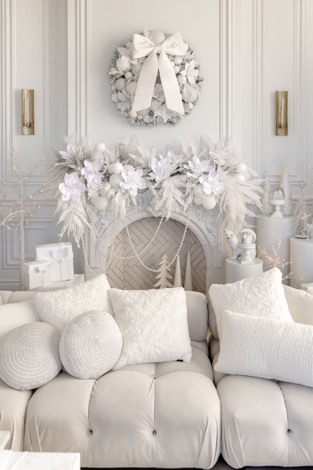 Elegant white Christmas decor featuring a plush tufted couch, decorative pillows, and a wreath adorned with a white bow.